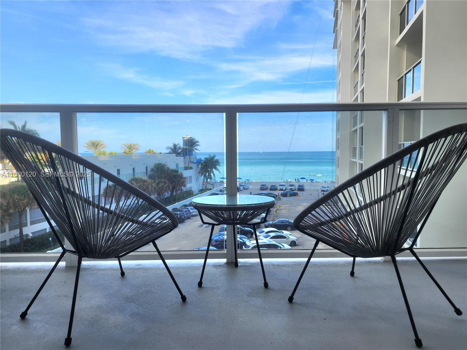 A balcony features two cord chairs and a small table overlooking the ocean and parking — 3505 S Ocean Dr # 407, Hollywood FL 33019, HOLLYWOOD, FL