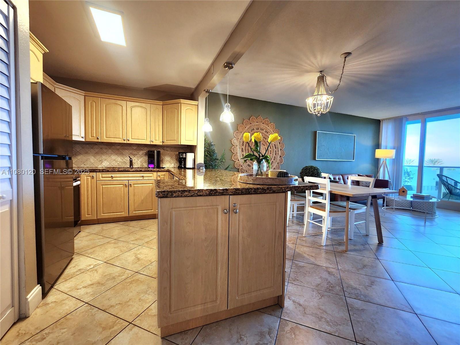 A kitchen with light wood cabinets and granite countertops opens into a dining area — 3505 S Ocean Dr # 407, Hollywood FL 33019, HOLLYWOOD, FL
