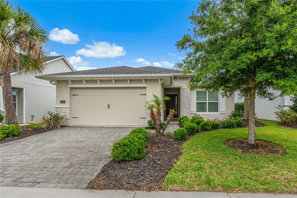 A single-story house with a beige garage, stone accents, and a paved driveway — 6243 WOODHAVEN VILLAGE DRIVE, PORT ORANGE, FL