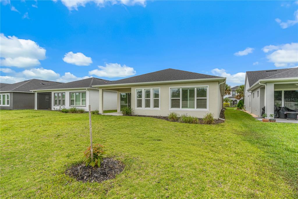 The exterior rear view of a suburban house features a covered patio and grassy yard — 6243 WOODHAVEN VILLAGE DRIVE, PORT ORANGE, FL