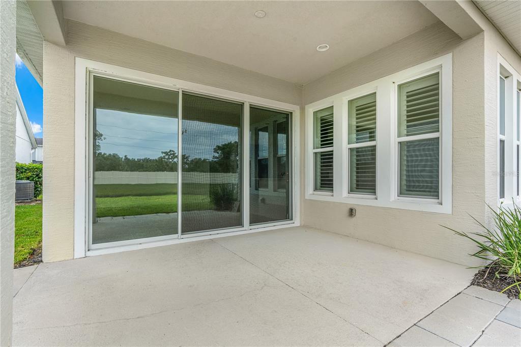 A covered concrete patio features a large sliding glass door and three adjacent windows — 6243 WOODHAVEN VILLAGE DRIVE, PORT ORANGE, FL