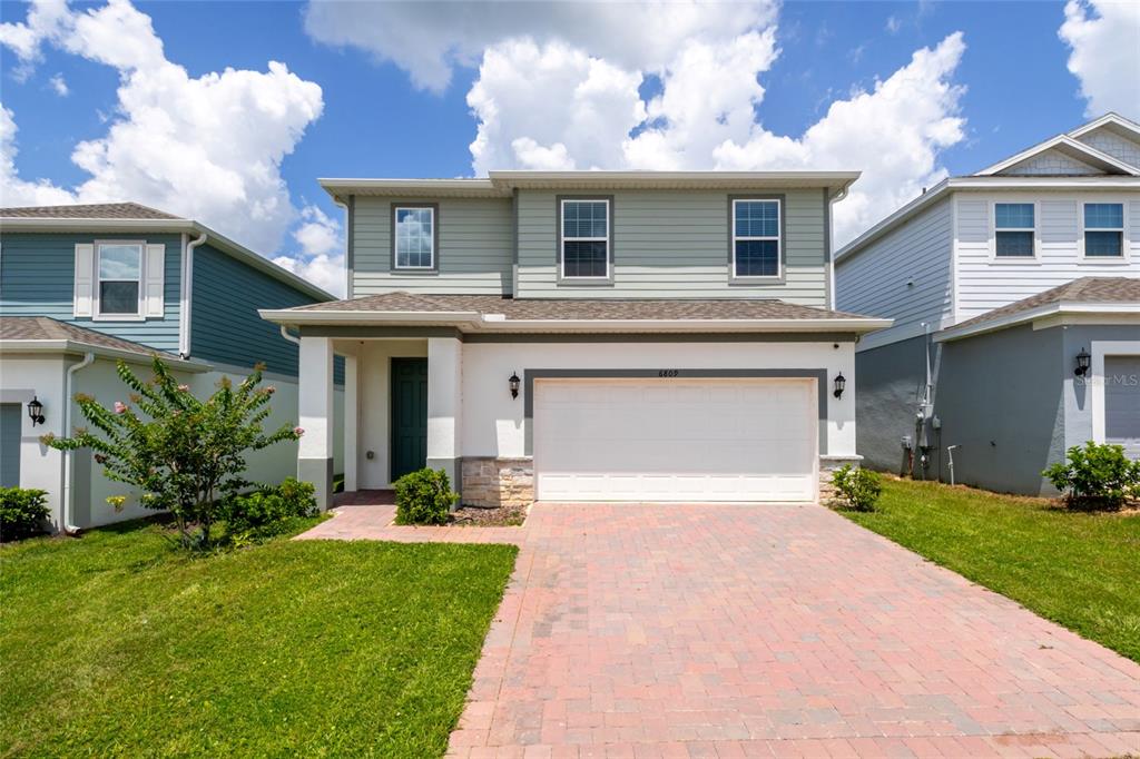 A two-story suburban house features a light-colored facade, a two-car garage, and a paved driveway — 6809 SERPENT HAWK LANE, HOWEY IN THE HILLS, FL