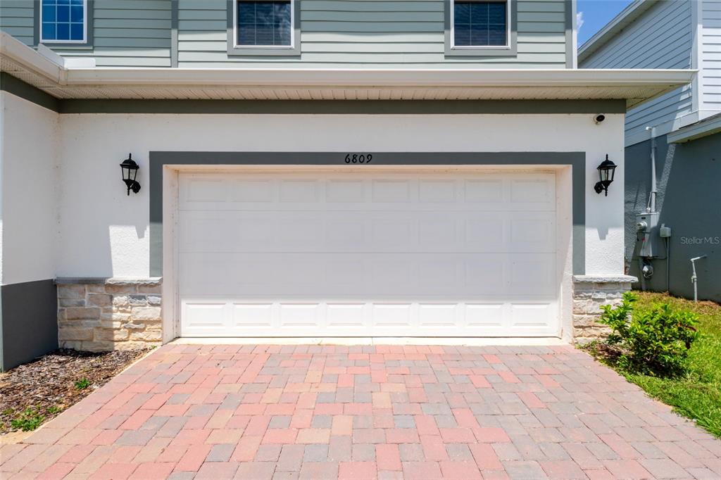 A white two-car garage door with a paved driveway and stone accents on the exterior — 6809 SERPENT HAWK LANE, HOWEY IN THE HILLS, FL