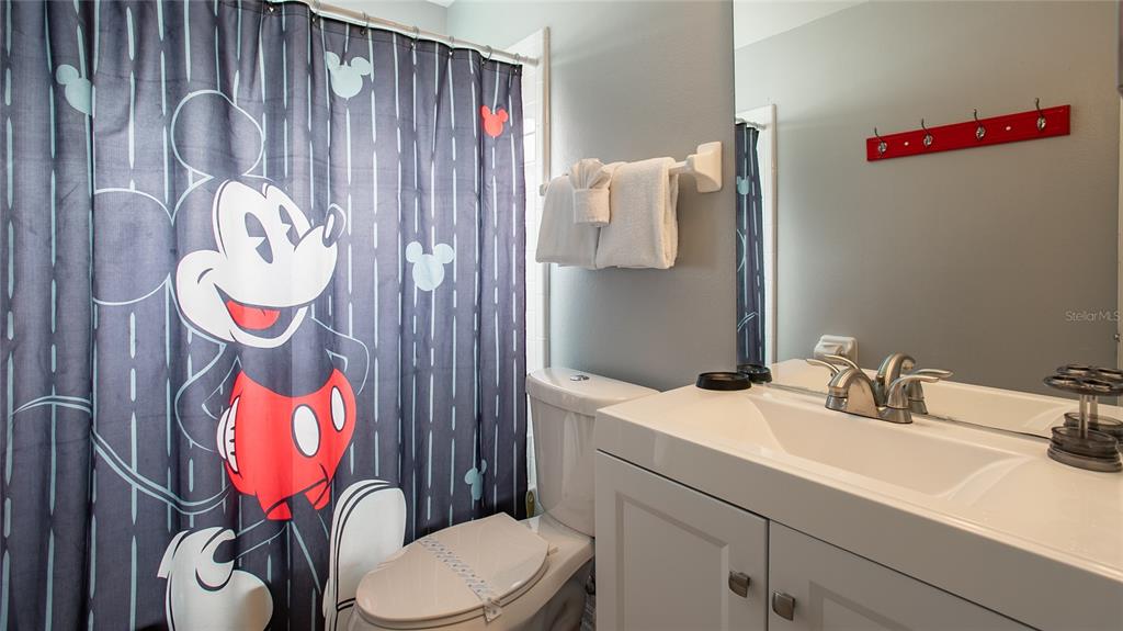 A bathroom features a Mickey Mouse shower curtain, a white vanity, and a red towel rack — 7802 LAUREL OAK LANE, KISSIMMEE, FL