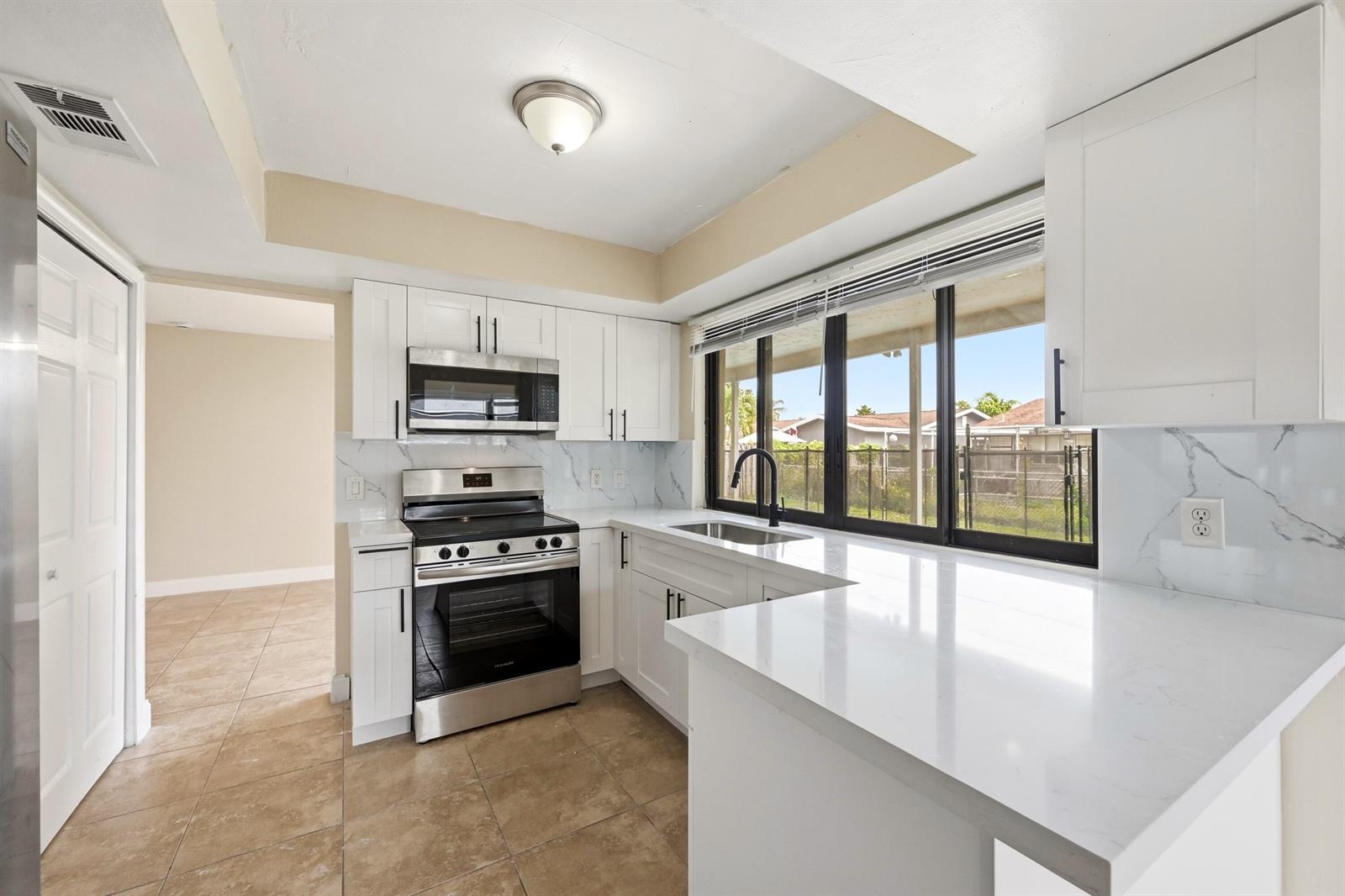 A single-story house features a light gray exterior, a large asphalt driveway, and a tree — 9671 NW 24th Street, Sunrise FL 33322, SUNRISE, FL