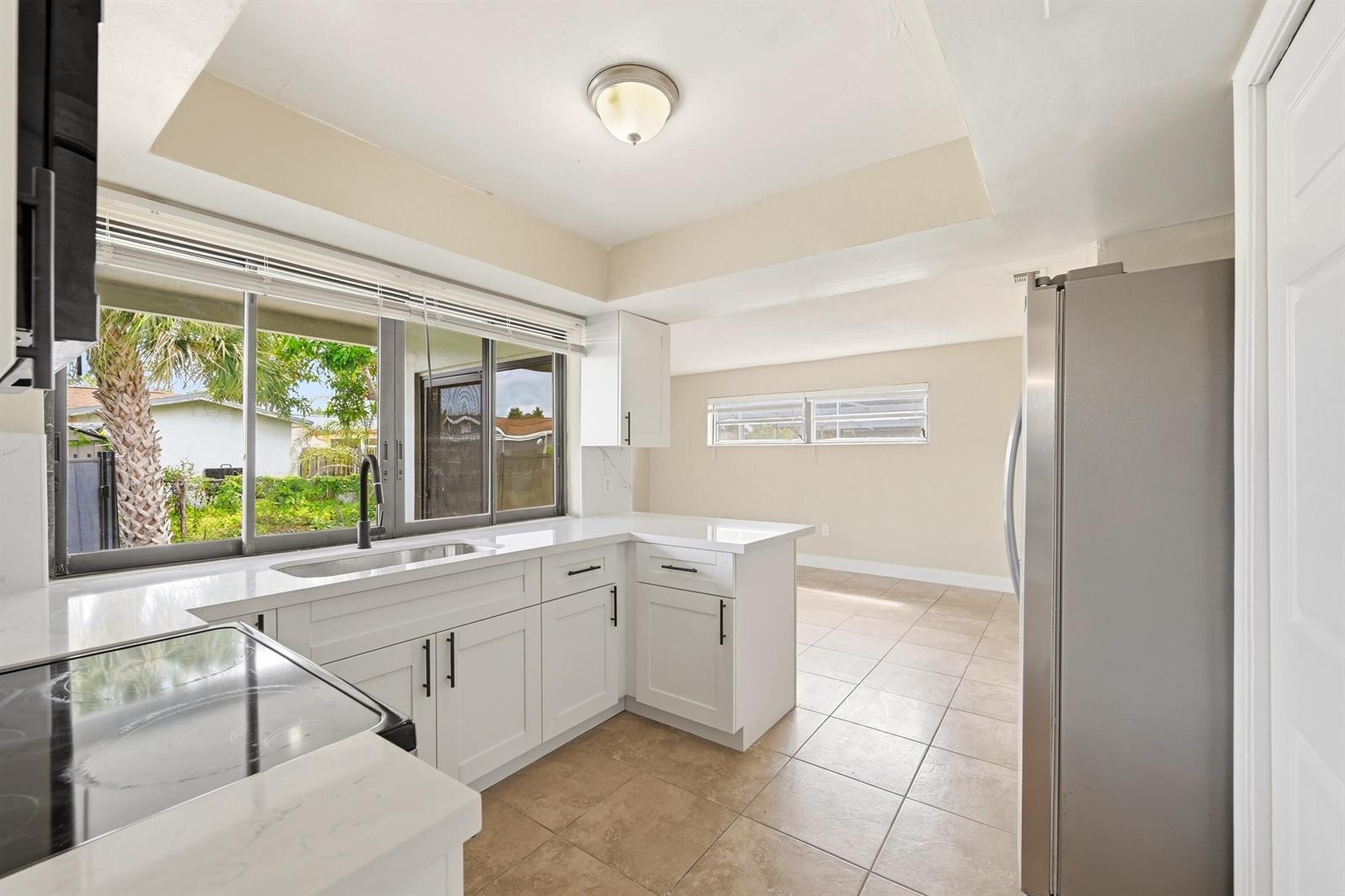 A kitchen features white cabinets, quartz countertops, stainless steel appliances, and a window view — 9671 NW 24th Street, Sunrise FL 33322, SUNRISE, FL