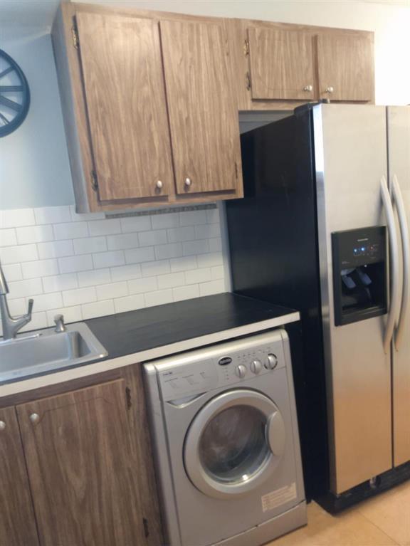 A kitchen features wood-grain cabinets, a stainless steel refrigerator, a washing machine, and subway tile — 8001 Crespi Boulevard # 5c, Miami Beach FL 33141, MIAMI BEACH, FL