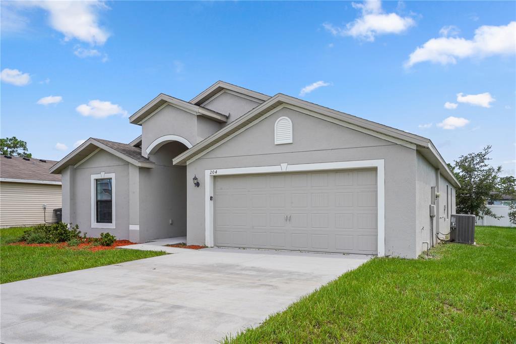 A single-story house with a gray stucco exterior, a two-car garage, and a concrete driveway — 204 HYACINTH COURT, POINCIANA, FL
