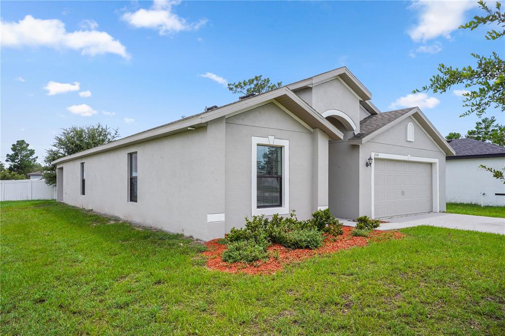 A single-story house with a gray stucco exterior, a two-car garage, and a front lawn — 204 HYACINTH COURT, POINCIANA, FL