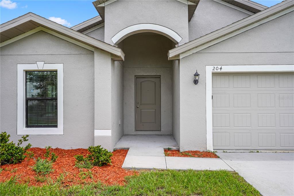 The exterior of a gray house features a front door, a garage, and red mulch — 204 HYACINTH COURT, POINCIANA, FL