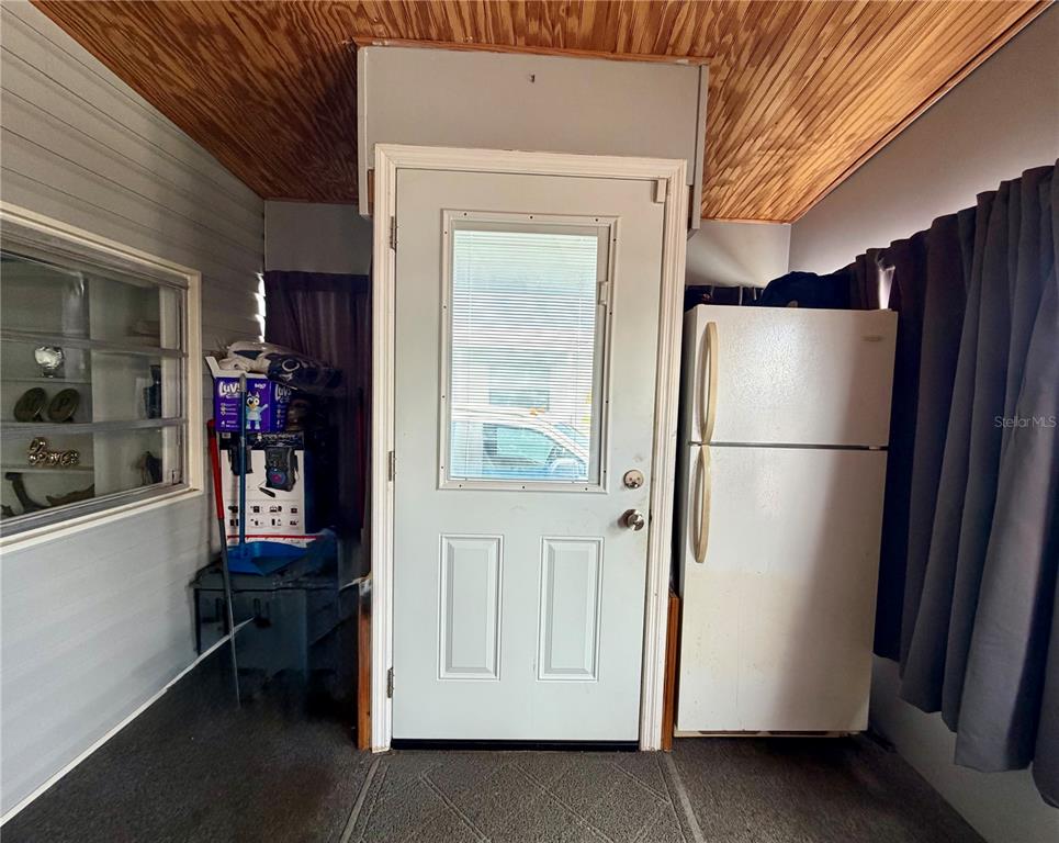 A room with wood-paneled ceiling, gray walls, a white exterior door, and a refrigerator — 916 51ST AVENUE PLAZA W, BRADENTON, FL