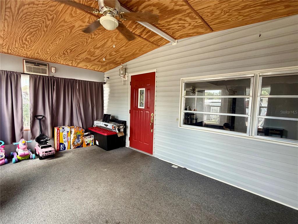 A covered porch features gray siding, a red door, a wood-paneled ceiling, and carpeted flooring — 916 51ST AVENUE PLAZA W, BRADENTON, FL