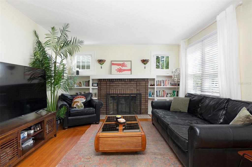 A living room features a brick fireplace, built-in bookshelves, a black leather sofa, and hardwood floors — 540 11TH AVENUE N, ST PETERSBURG, FL