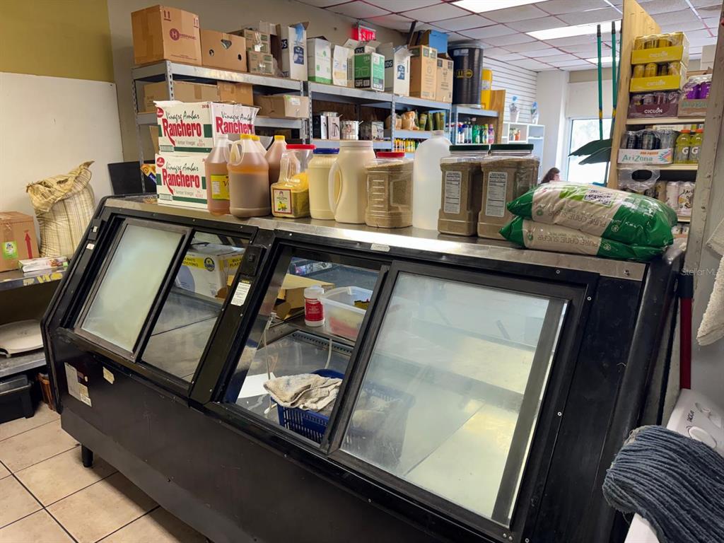 A commercial kitchen area features a large refrigerated display case topped with various food supplies — 131 BUENAVENTURA BOULEVARD UNIT 1A, KISSIMMEE, FL