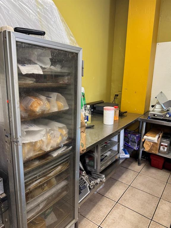 A commercial kitchen area features a tall glass-front refrigerator, stainless steel counters, and tiled flooring — 131 BUENAVENTURA BOULEVARD UNIT 1A, KISSIMMEE, FL