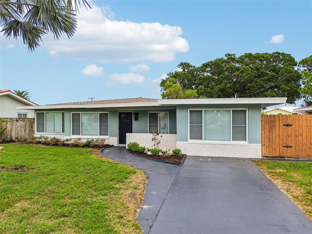 A single-story house with a light blue exterior, a dark driveway, and a wooden fence — 403 DRIFTWOOD DRIVE W, PALM HARBOR, FL