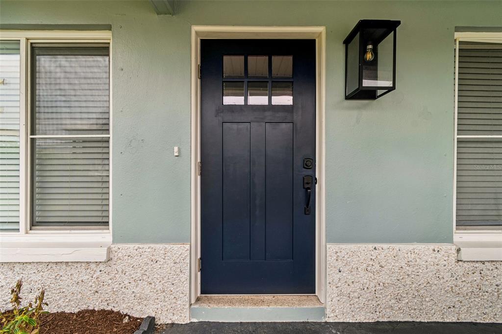 A dark blue front door with a window pane sits between two windows on a house — 403 DRIFTWOOD DRIVE W, PALM HARBOR, FL