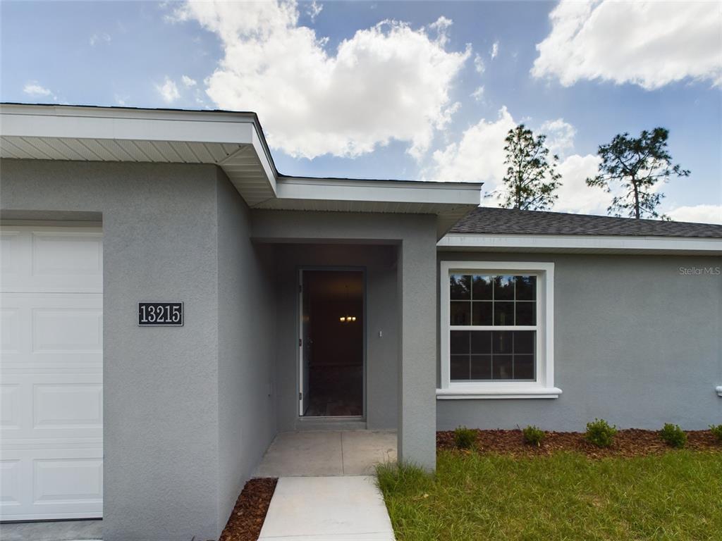 The exterior of a gray house features a white garage door, front entrance, and window — 13215 SW 77TH AVENUE, OCALA, FL