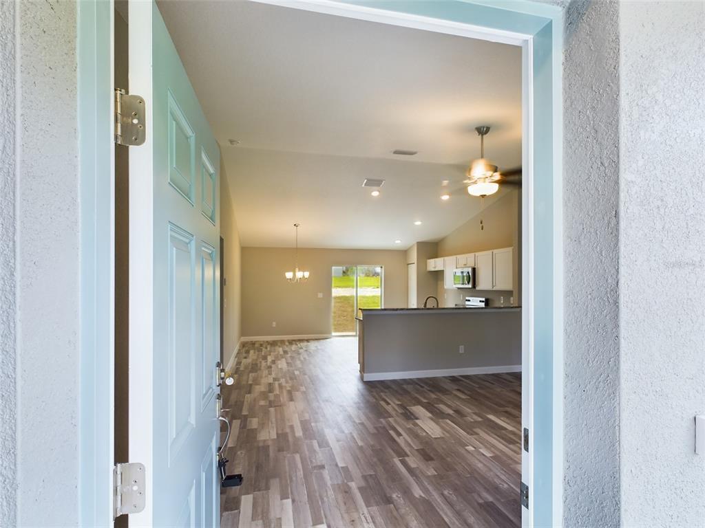A view through an open front door into an open-concept living area with wood flooring — 13215 SW 77TH AVENUE, OCALA, FL