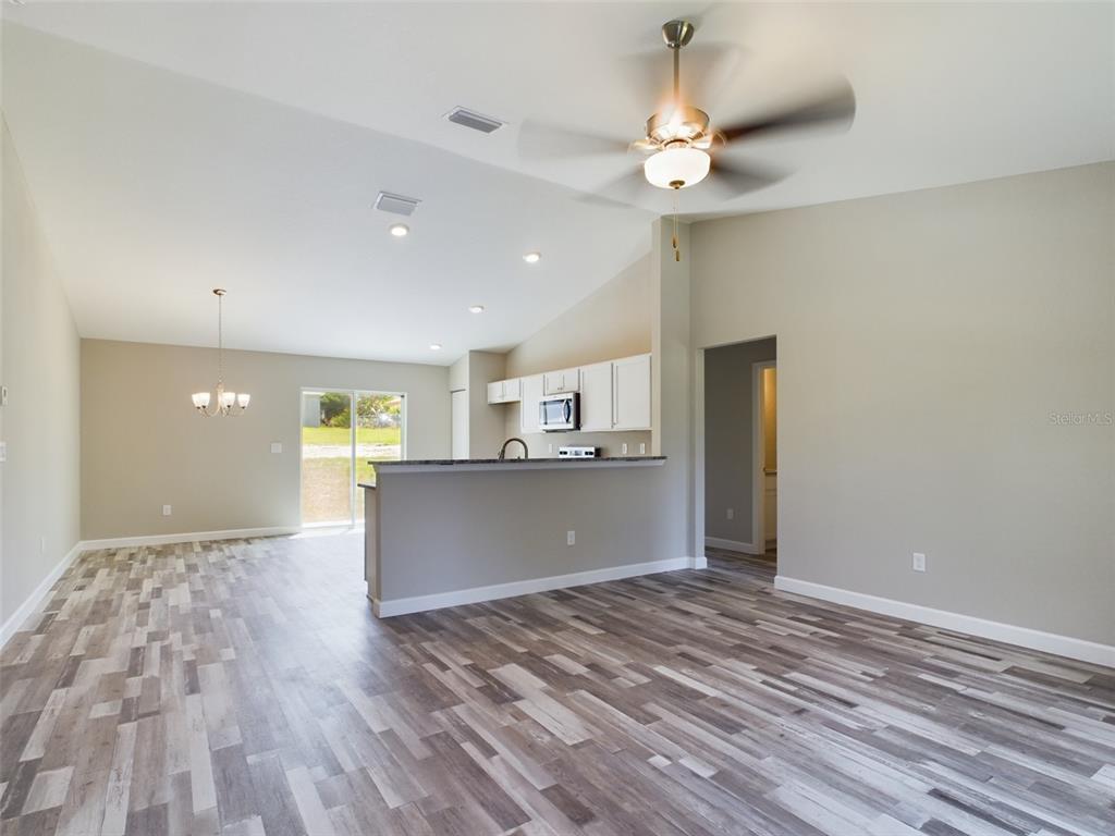 An open-concept living area features wood-look flooring, a kitchen island, and a sliding glass door — 13215 SW 77TH AVENUE, OCALA, FL