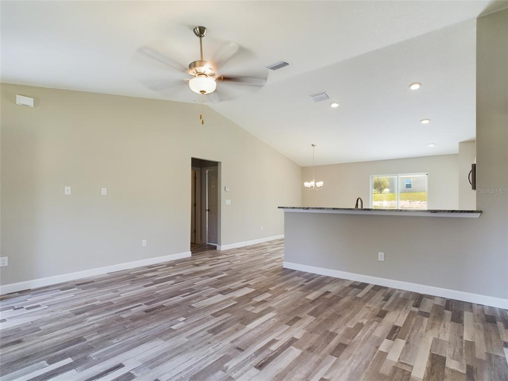 An open-concept living area features vaulted ceilings, a ceiling fan, and wood-look laminate flooring — 13215 SW 77TH AVENUE, OCALA, FL