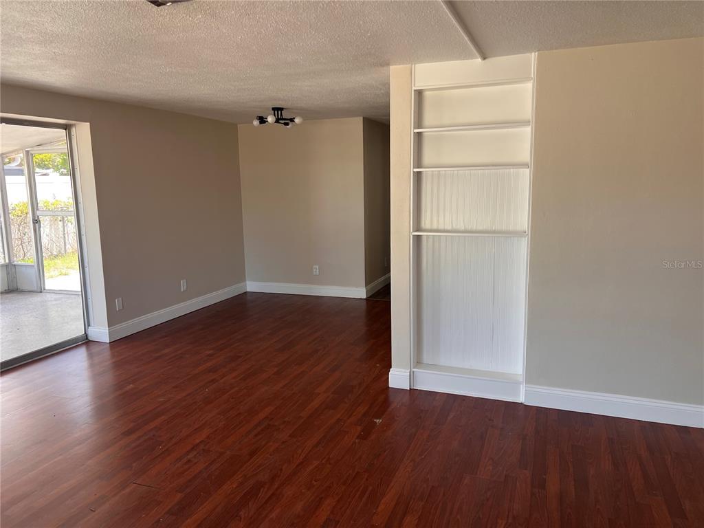 An empty living room features dark wood flooring, beige walls, and a built-in white bookshelf — 6111 ROLLINS STREET, BRADENTON, FL