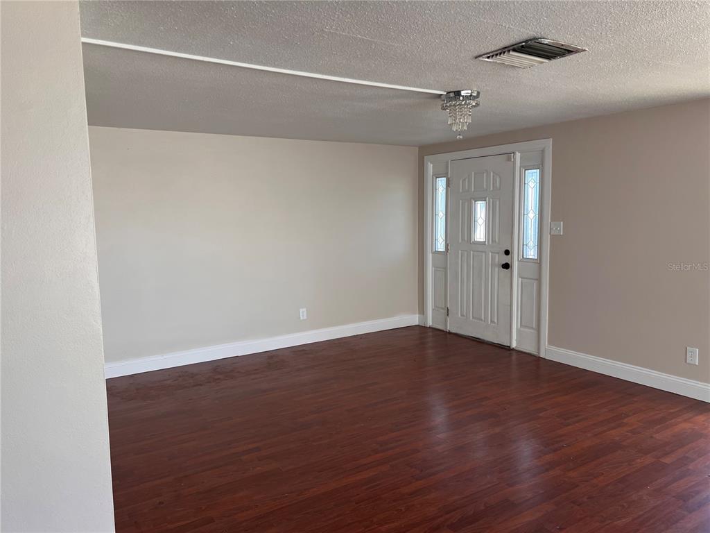 An empty room with dark wood flooring, beige walls, and a white front door — 6111 ROLLINS STREET, BRADENTON, FL
