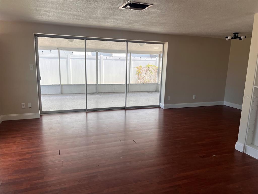 An empty room features dark wood-look flooring, beige walls, and large sliding glass patio doors — 6111 ROLLINS STREET, BRADENTON, FL