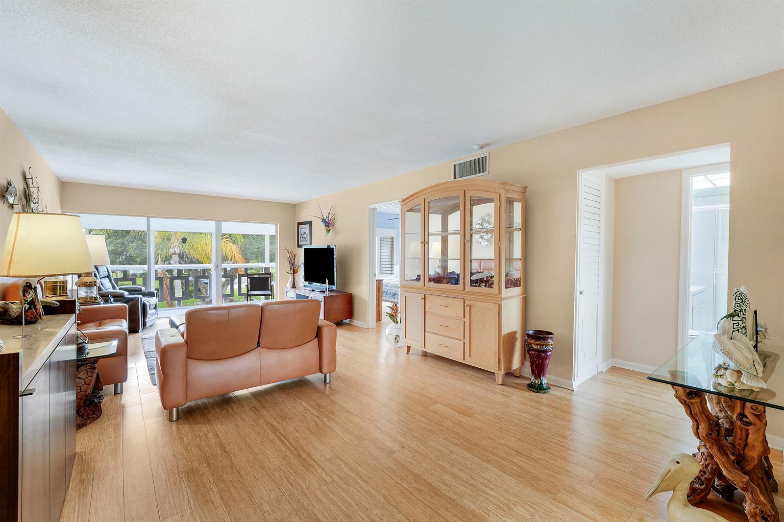 A living room features light wood flooring, a tan leather sofa, and a wooden china cabinet — 331 Tequesta Drive # 213, Tequesta FL 33469, TEQUESTA, FL