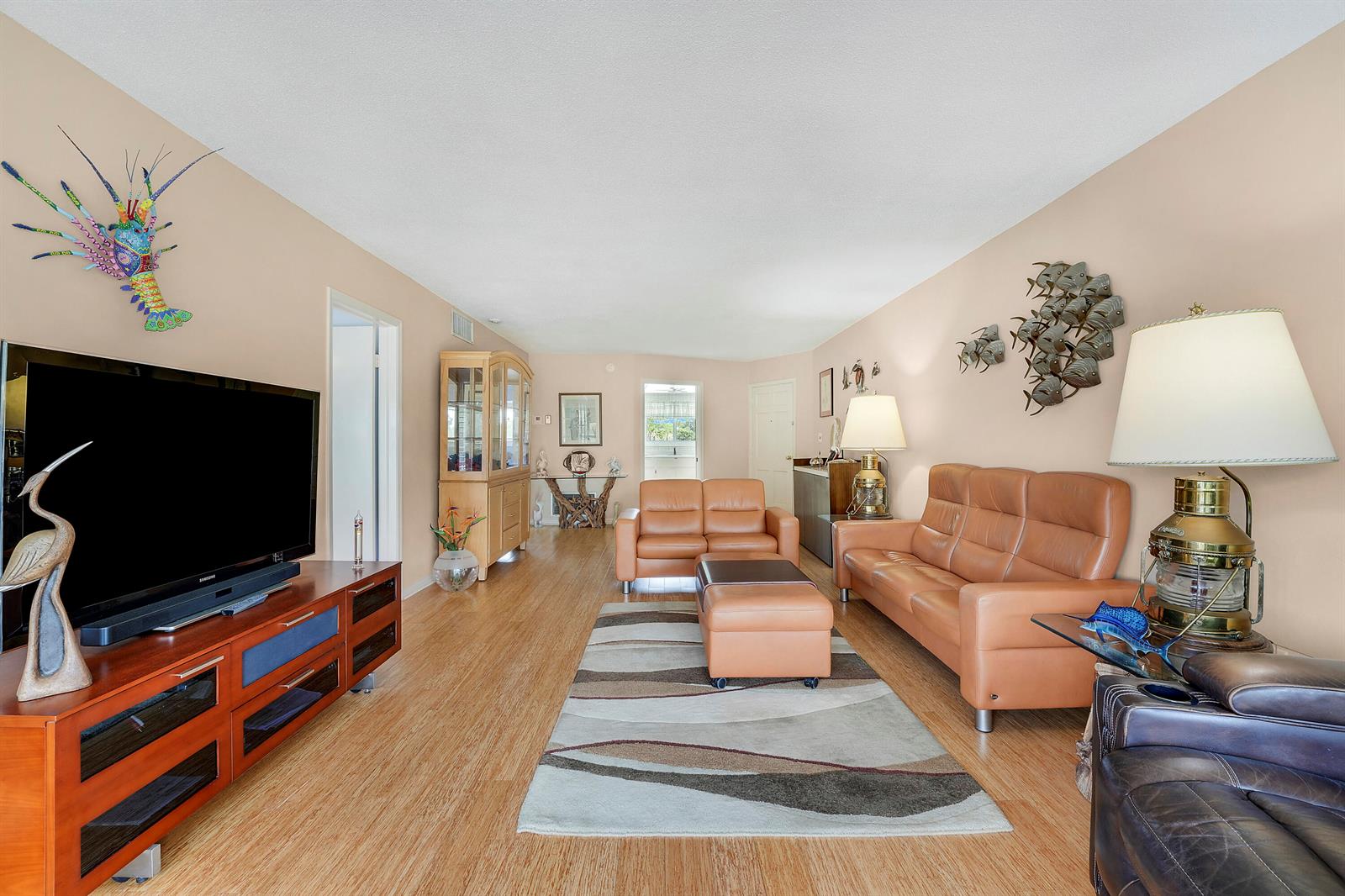 A living room features light wood flooring, tan walls, leather furniture, and nautical-themed wall decor — 331 Tequesta Drive # 213, Tequesta FL 33469, TEQUESTA, FL
