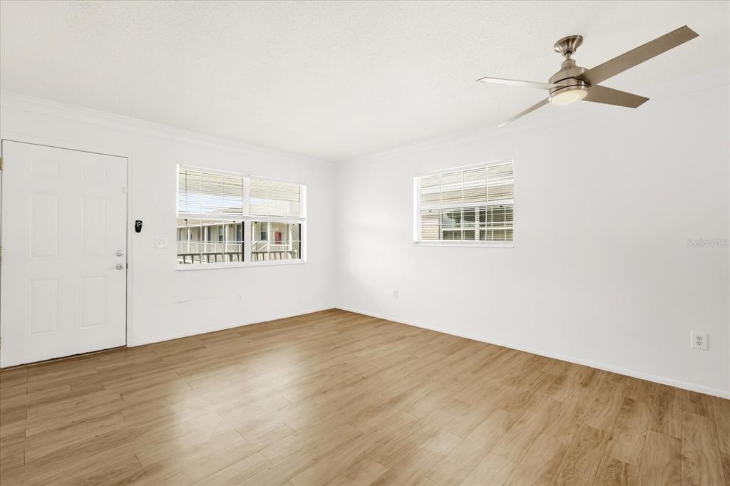 An empty room with white walls, light wood-look flooring, two windows, and a ceiling fan — 1400 EUDORA RD UNIT F57, MOUNT DORA, FL