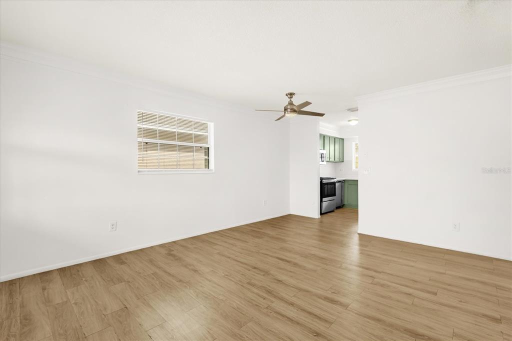 A bright living room features light wood-look flooring, white walls, and a ceiling fan — 1400 EUDORA RD UNIT F57, MOUNT DORA, FL
