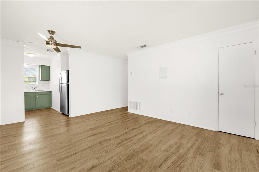 A room with light wood-look flooring, white walls, a ceiling fan, and an adjacent kitchen — 1400 EUDORA RD UNIT F57, MOUNT DORA, FL