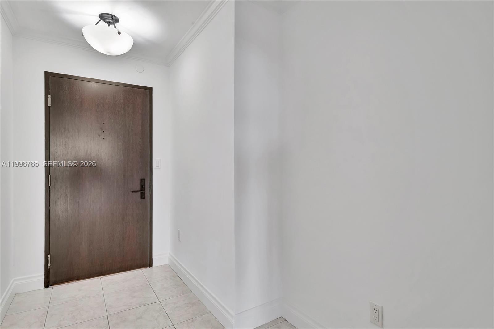 An entryway features a dark wood door, white walls, and light-colored tile flooring — 2901 S Bayshore Dr # 16G, Miami FL 33133, MIAMI, FL