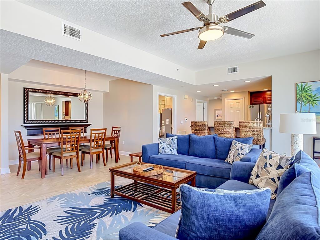 A living room and dining area feature blue sofas, a wooden coffee table, and tile flooring — 3799 S ATLANTIC AVENUE UNIT 1001, DAYTONA BEACH, FL