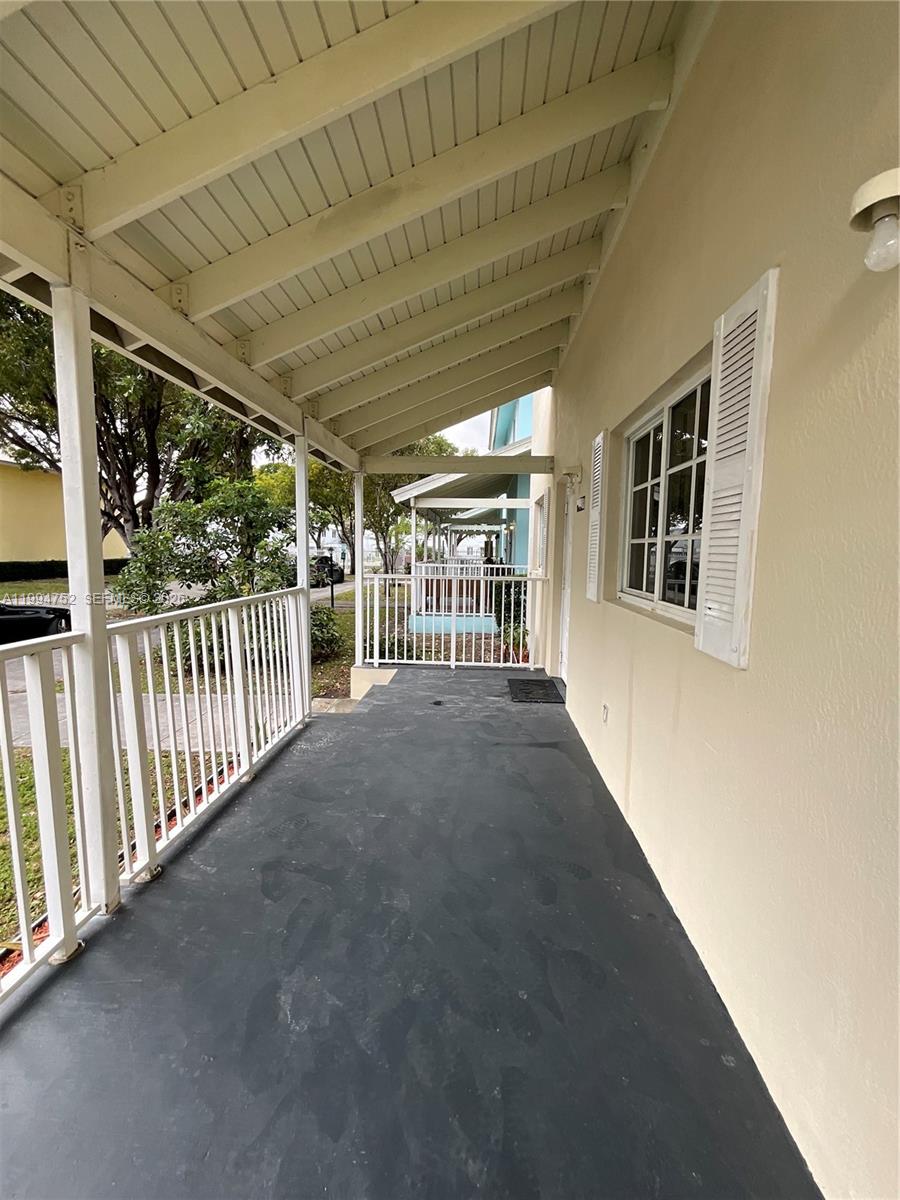 A covered porch with a dark painted floor, white railings, and a window with shutters — 435 NW 19th Ln # 19, Miami FL 33136, MIAMI, FL