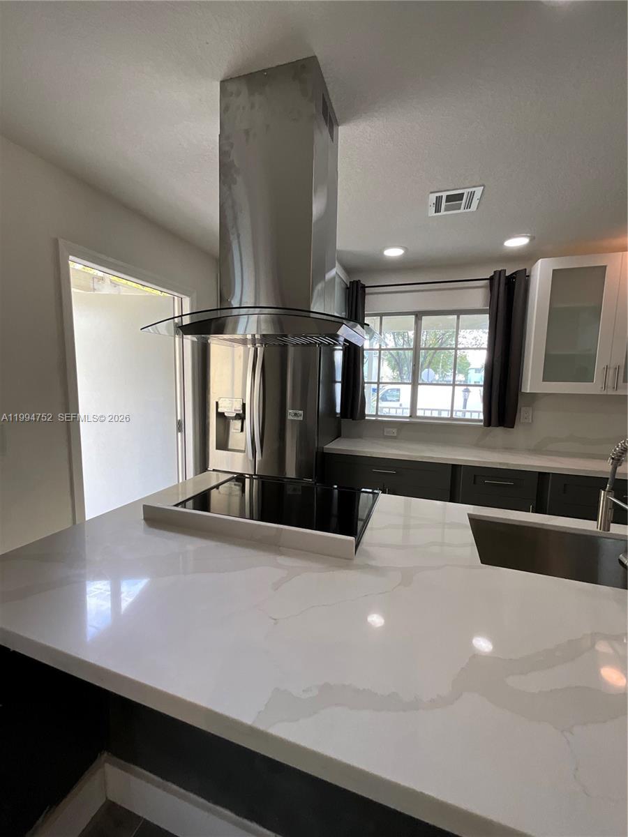 A kitchen features a central island with a cooktop, stainless steel hood, and quartz countertops — 435 NW 19th Ln # 19, Miami FL 33136, MIAMI, FL