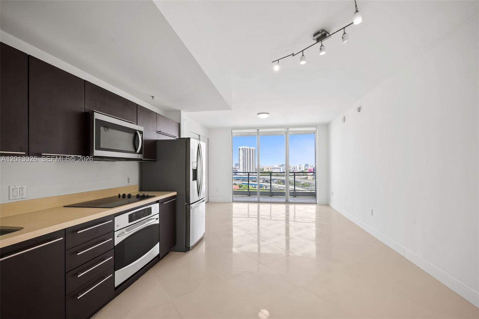 A modern kitchen with dark cabinets and stainless steel appliances opens to a bright living area — 90 SW 3rd St # 1608, Miami FL 33130, MIAMI, FL