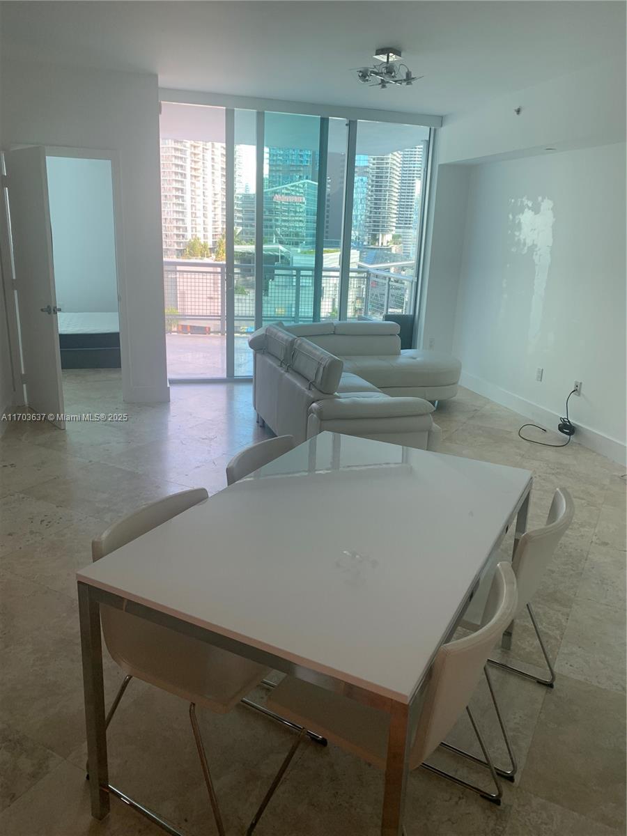 A dining area with a white table and chairs sits before a living room with a sofa — 350 S Miami Ave # 1704, Miami FL 33130, MIAMI, FL