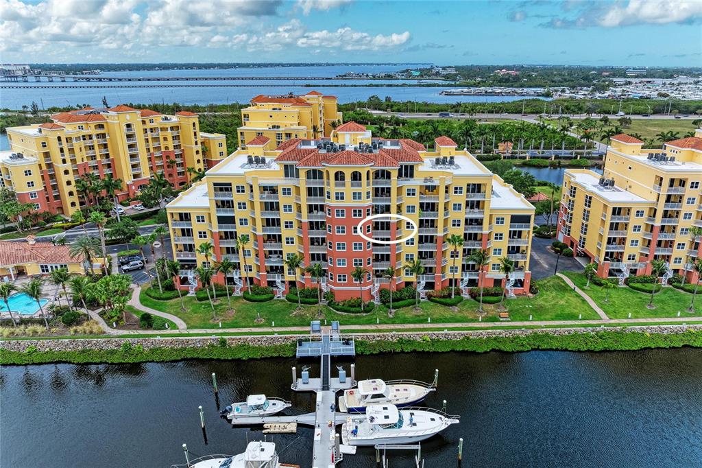 An aerial view shows a multi-story yellow apartment complex with a circled balcony overlooking water — 610 RIVIERA DUNES WAY UNIT 404, PALMETTO, FL