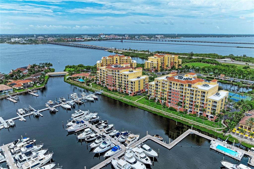 An aerial view shows a marina with docked boats beside multi-story residential buildings and water — 610 RIVIERA DUNES WAY UNIT 404, PALMETTO, FL