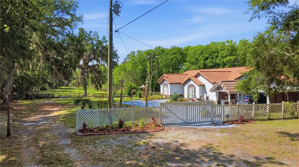 A white house with a terracotta tile roof sits behind a white lattice fence — 1898 BLACKWELDER ROAD, DE LEON SPRINGS, FL