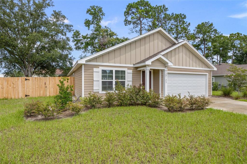 A tan, single-story suburban house with a two-car garage and a wooden fence — 20105 NW 247TH STREET, HIGH SPRINGS, FL