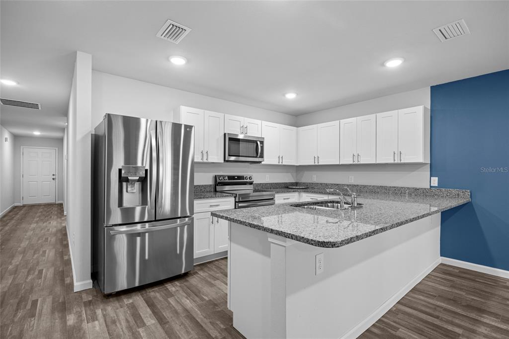 A kitchen features white cabinets, granite countertops, stainless steel appliances, and a blue accent wall — 20105 NW 247TH STREET, HIGH SPRINGS, FL