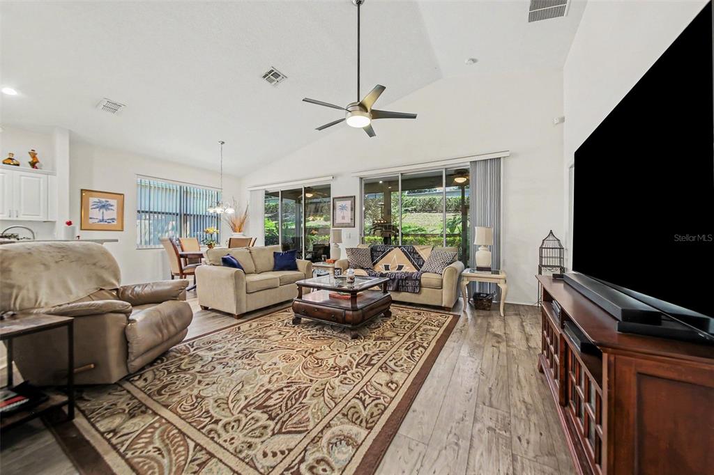 A living room with wood-look flooring, a large area rug, and a vaulted ceiling — 2361 PRAIRIE DUNES, CLERMONT, FL