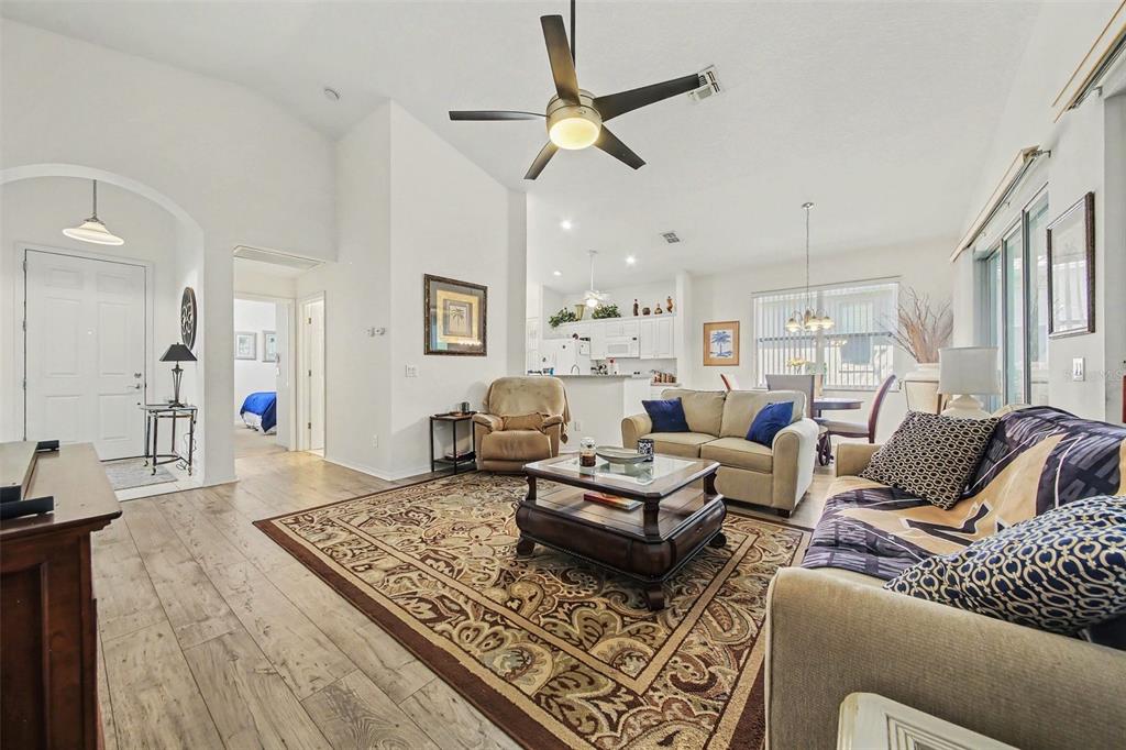 A living room with wood-look flooring, a ceiling fan, and an open kitchen in back — 2361 PRAIRIE DUNES, CLERMONT, FL