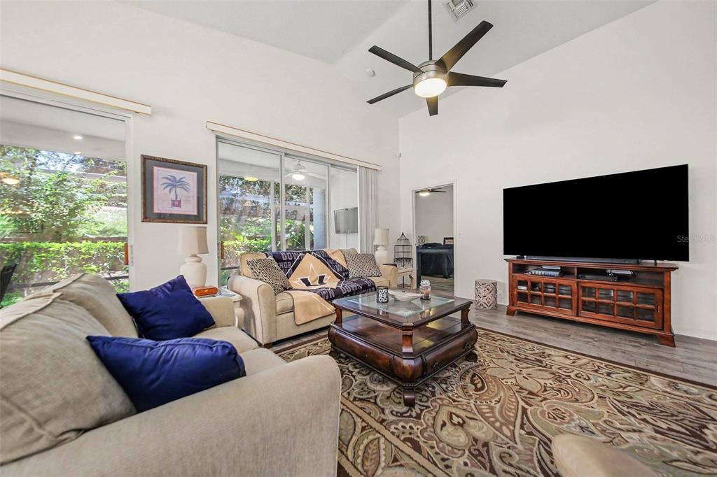 A living room features a vaulted ceiling, a ceiling fan, and a large television console — 2361 PRAIRIE DUNES, CLERMONT, FL