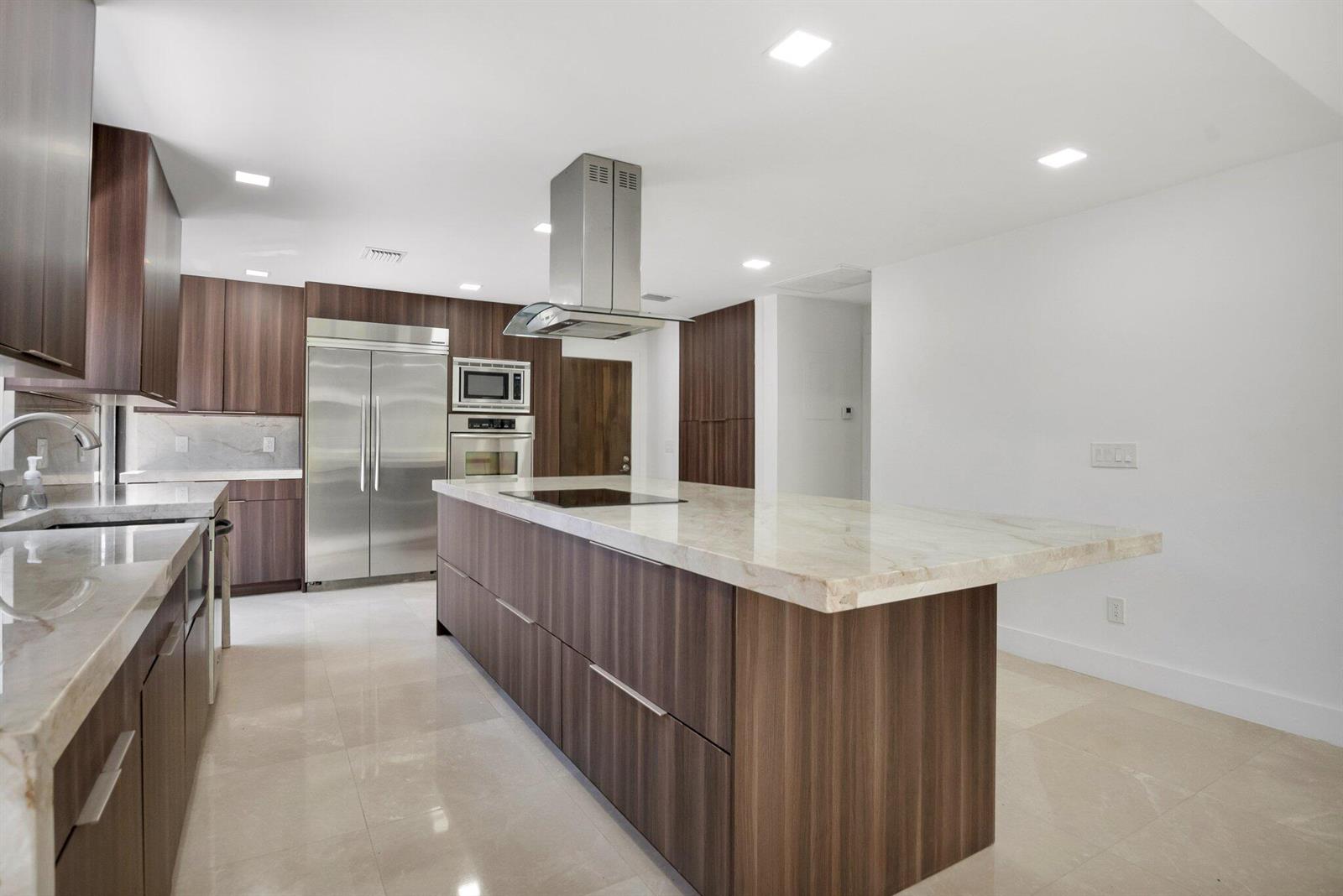A modern kitchen features dark wood cabinetry, a large marble-topped island, and stainless steel appliances — 21922 Cypress Drive, Boca Raton FL 33433, BOCA RATON, FL