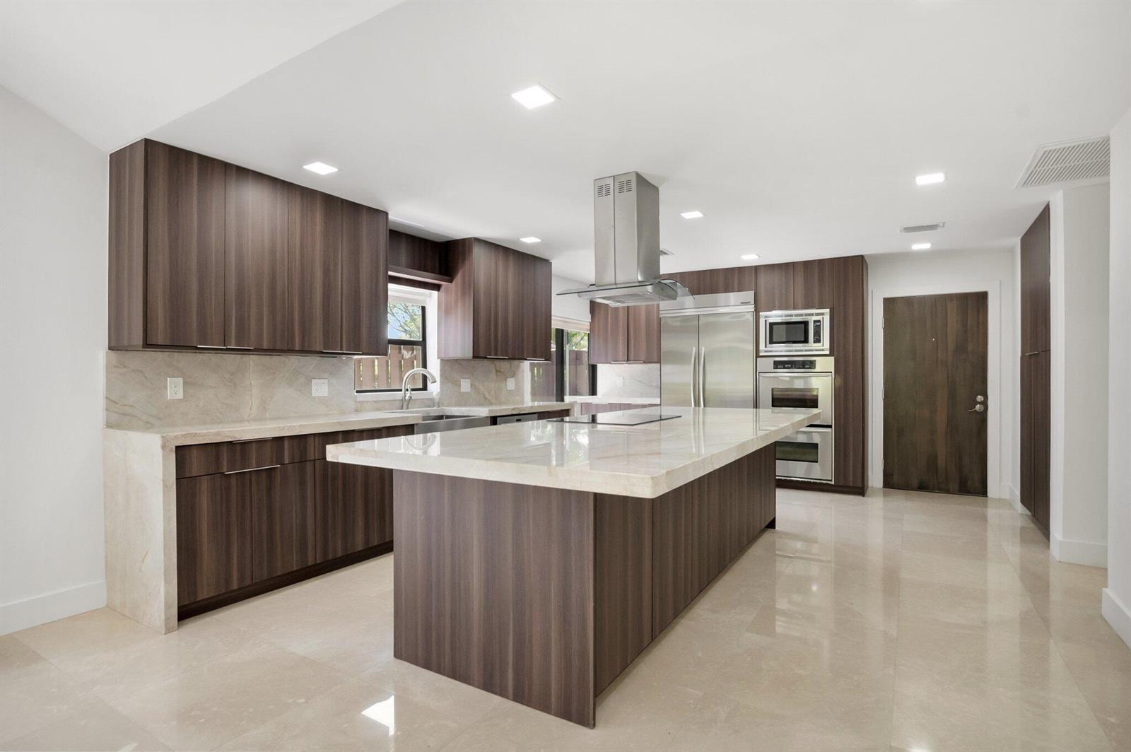 A modern kitchen features dark wood cabinetry, a large stone island, and stainless steel appliances — 21922 Cypress Drive, Boca Raton FL 33433, BOCA RATON, FL