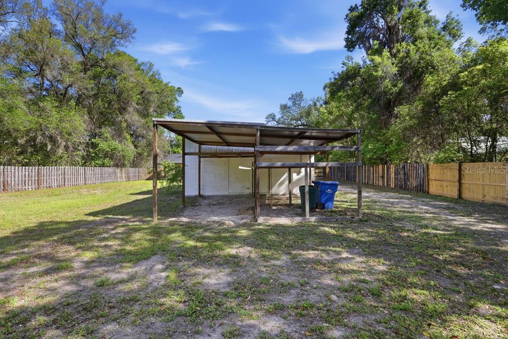A backyard features a white concrete block shed with an attached metal-roofed carport — 550 E MINNESOTA AVENUE, ORANGE CITY, FL